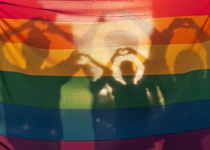 Siluetter som bildar hjärtform med händer mot prideflagga